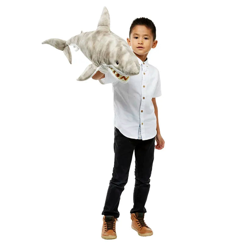 A young boy in a white shirt and dark pants confidently holds The Puppet Company Large Creature Shark against a plain white background, with his neatly laced brown shoes suggesting he's set for creative play.