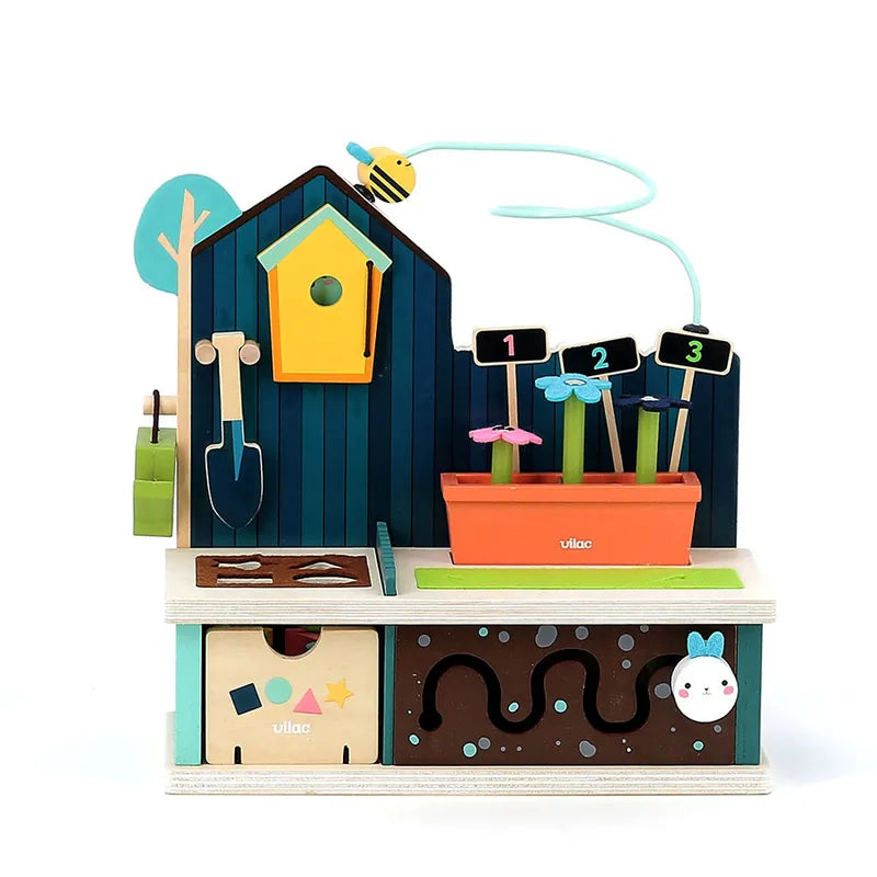 The Vilac Early Learning Garden is a vibrant wooden activity toy designed for children aged 18 months and older. It features a blue house with a birdhouse, a tree, and gardening tools. Below, there is a flower box with numbered flowers, a compost bin, and a worm maze. Additionally, there's a bee on a wire that can slide across the top.