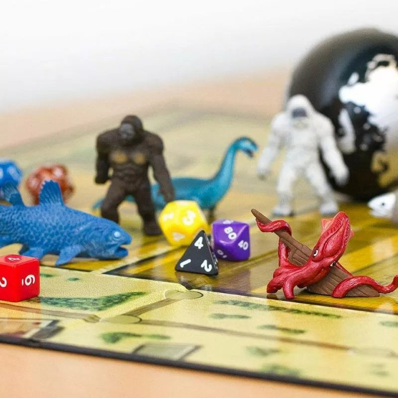 A board game with colorful dice, plastic dinosaur and monster figurines, a globe, and a map-like board, suggesting a fun, adventurous game in progress.