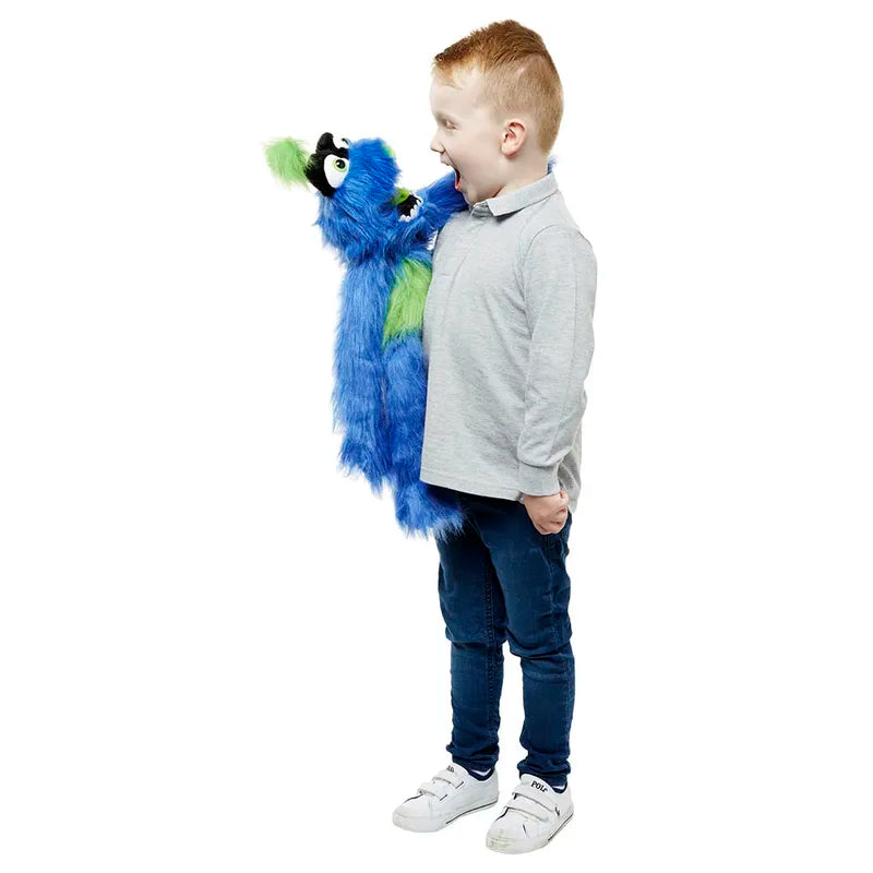 A smiling child stands holding The Puppet Company Blue Monster, a vibrant puppet known for its large, expressive eyes. It seems to be playfully interacting with the child against a plain white background.