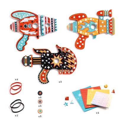 The Djeco Mosaics & Stickers Kosmik kit includes three vibrant wooden toy space blasters with detailed designs. The set also features four rubber bands, a variety of small accessories, and five sheets of decorative mosaic stickers in assorted colors and patterns. The toys are designed in orange, red, and black hues with star, circle, and zigzag motifs.