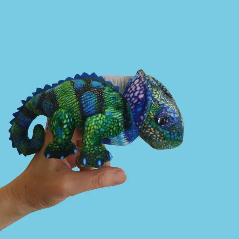 A hand holds The Puppet Company Chameleon (Blue-Green) Finger Puppet – Little Creatures Range, its vibrant green and blue scales standing out against a plain light blue background, showcasing the playful charm of this soft toy.