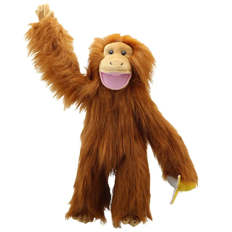 The Puppet Company Medium Puppet Primate Orangutan, featuring long orange-brown fur, is shown waving one arm while holding a banana in the other hand. It sports a large pink smile, ideal for simulating mouth movements during your playful adventures.