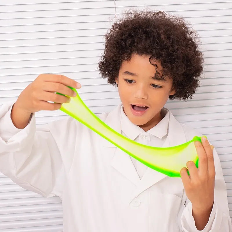 A child in a white lab coat stretches bright green Sentosphere Slime Workshop slime between their hands, looking amazed and curious. White striped background—perfect for a fun kids craft.