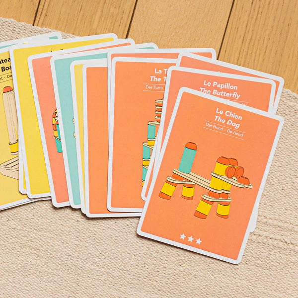 A set of bilingual Stix Construction Creative Cards flashcards with illustrations and text, laid out on a wooden surface.