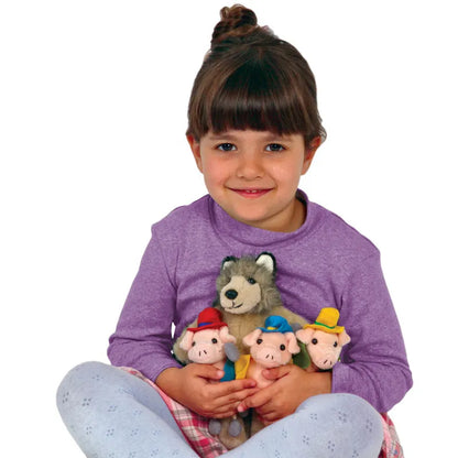 A young girl with brown hair in a bun smiles while sitting cross-legged. Dressed in a purple long-sleeved shirt and light blue patterned leggings, she holds The Puppet Company Finger Puppet Story Set: The Three Little Pigs, featuring plush toys of three pigs and a wolf, ready for storytelling. Perfect for bringing tales to life, it's as if they were made just for her.