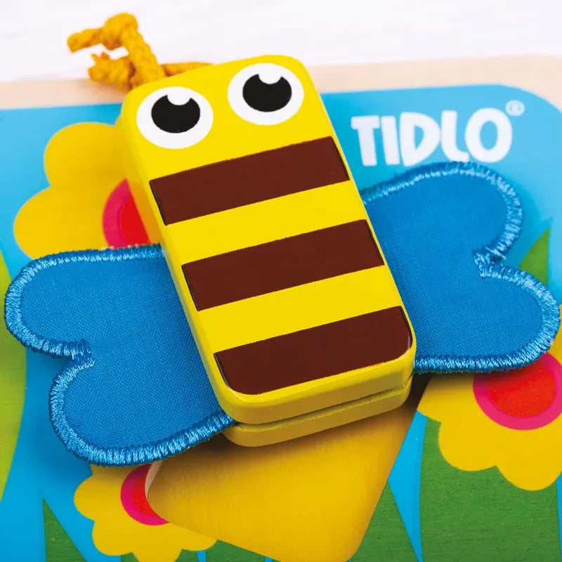A vibrant wooden "TIDLO" bee toy with yellow and brown stripes, big eyes, and blue wings rests on a flower-patterned background, enticing children to explore its textures. Part of the Touch and Feel Bugs Puzzle series.